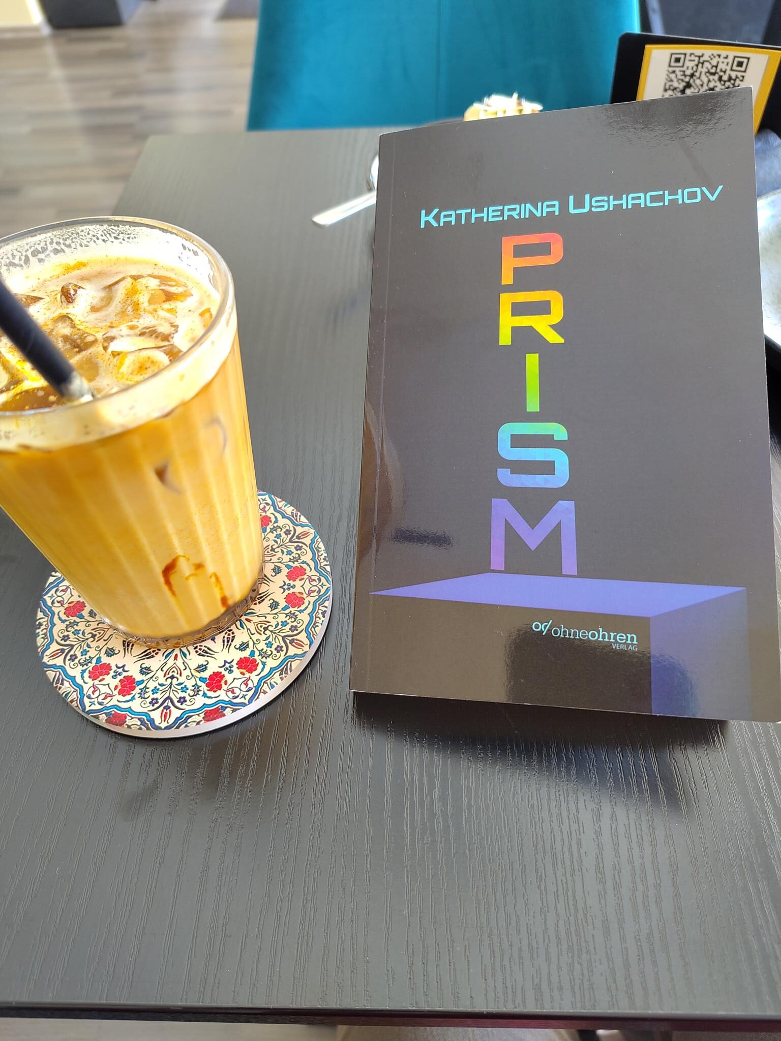 Foto vom Buch "Prism" neben einem Getränk.