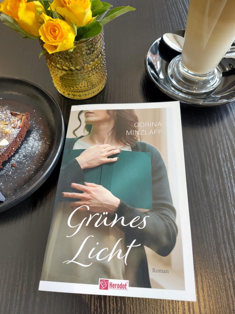 Foto vom Buch "Grünes Licht", neben Kuchen, Kaffee, und einer Blumenvase